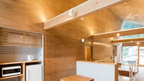 A modern kitchen with wooden cabinetry, a microwave, a refrigerator, and a wooden dining table with stools. - Mt.Takao Base Camp - Hostel (Hachioji)