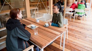 A wooden deck with tables and chairs, some occupied by people. - Mt.Takao Base Camp - Hostel (Hachioji)