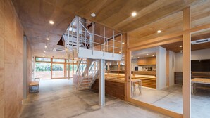 A spacious interior with a high ceiling, a mezzanine level, and large windows allowing natural light. - Mt.Takao Base Camp - Hostel (Hachioji)