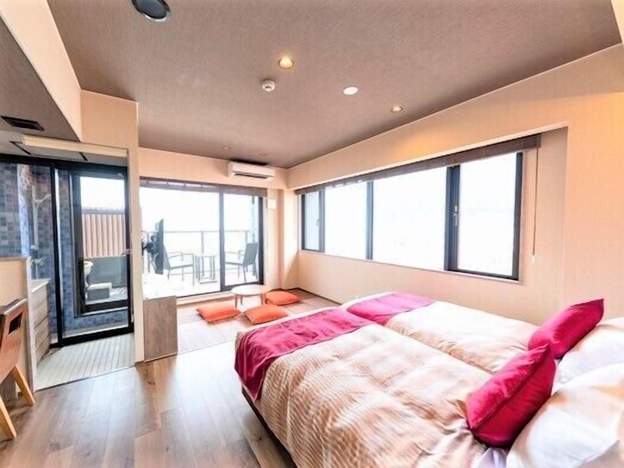 A modern bedroom with a bed, a desk, and a balcony with chairs.