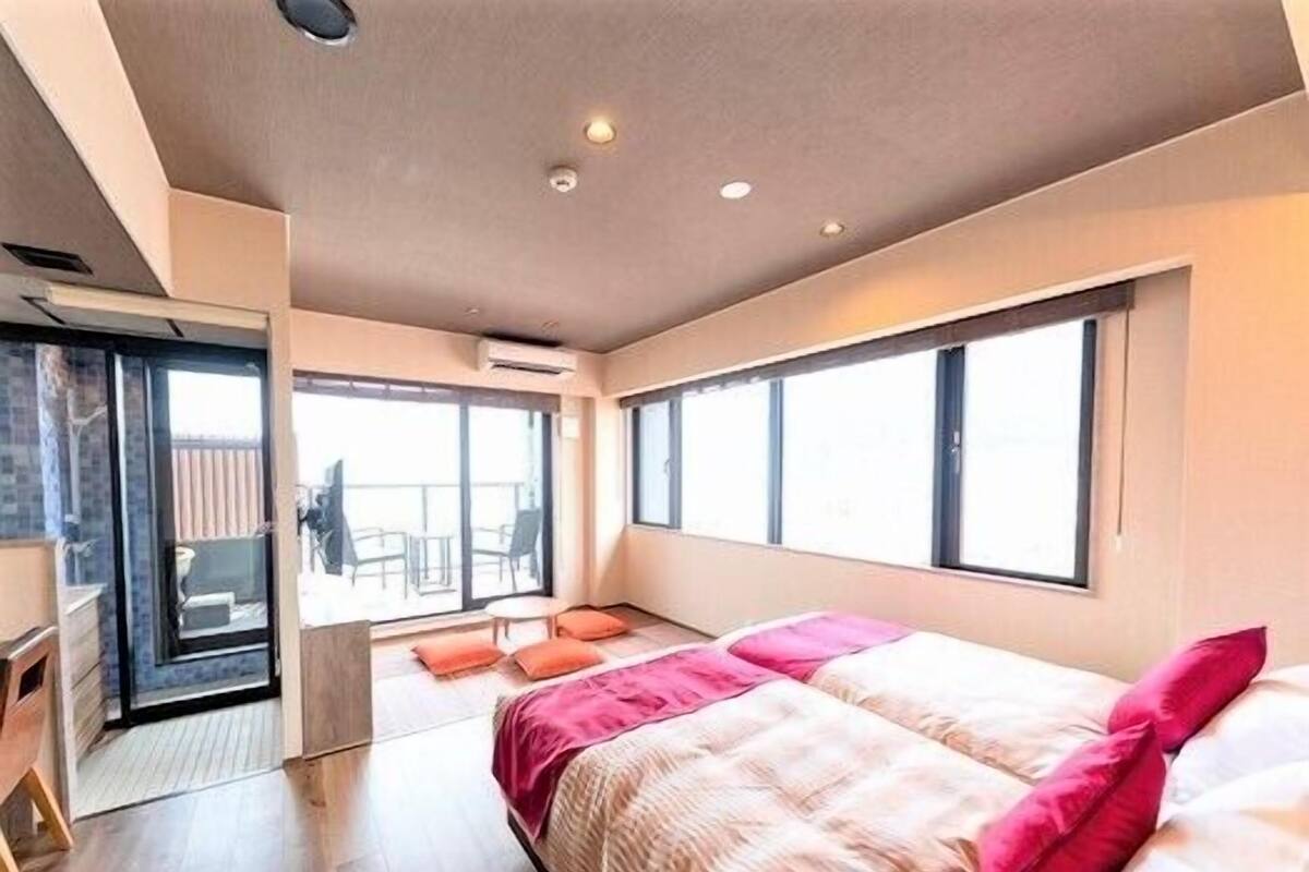 A modern bedroom with a bed, a desk, and a balcony with chairs.