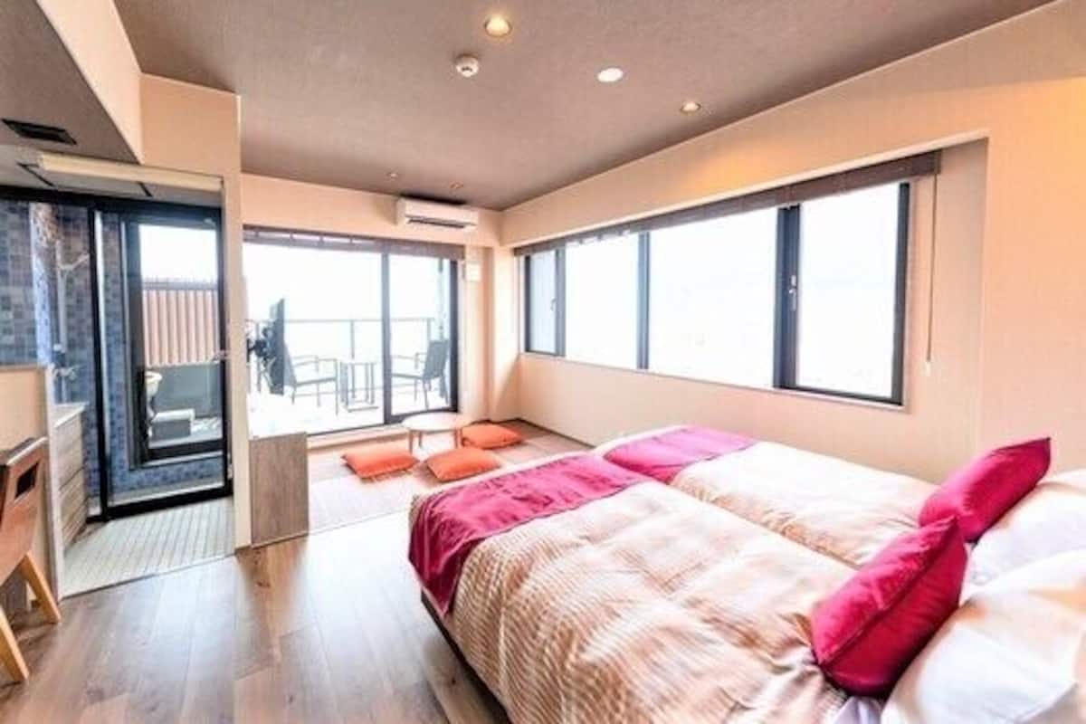 A modern bedroom with a bed, a desk, and a balcony with chairs.