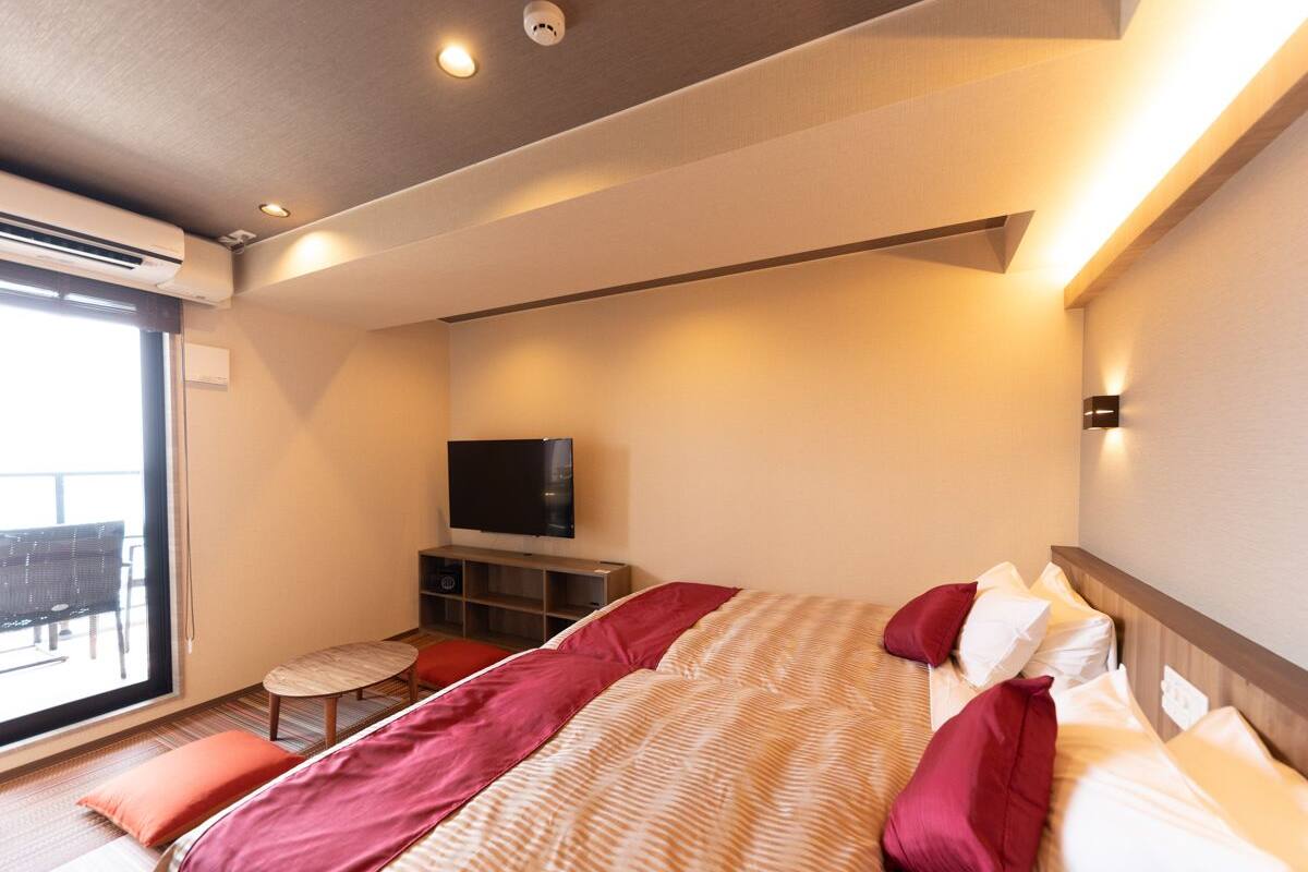 A modern hotel room with a large bed, a flat-screen TV, a small table, and a balcony.