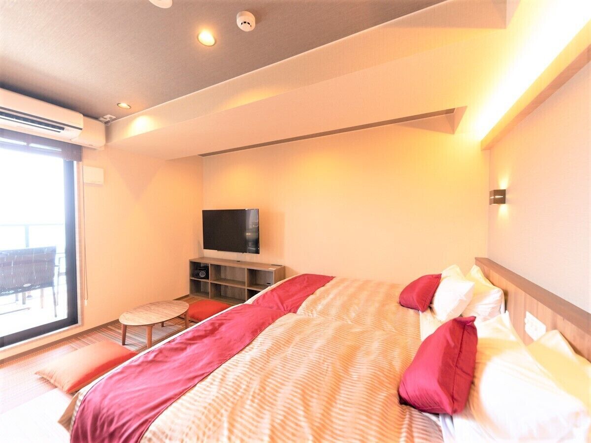 A hotel room with a bed, a TV, a small table, and a balcony.