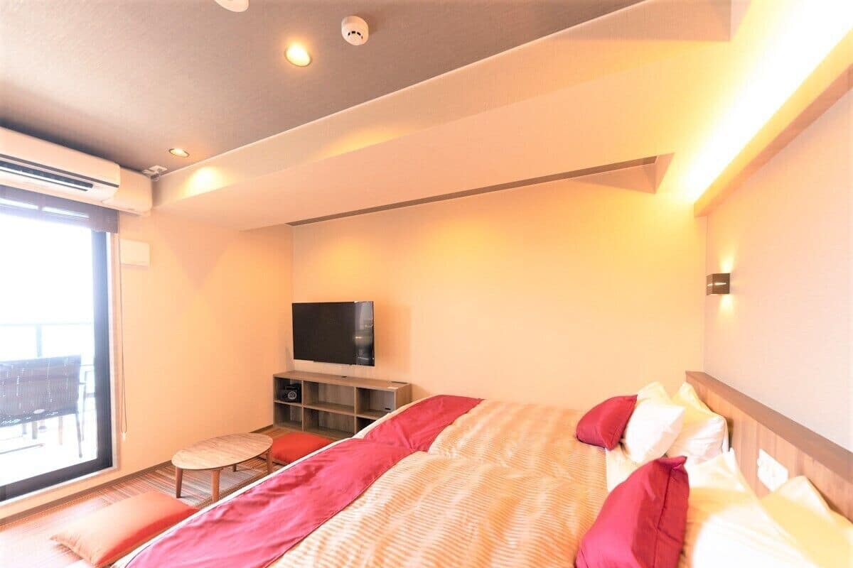 A hotel room with a bed, a TV, a small table, and a balcony.