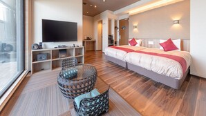 A modern hotel room with a large bed, a flat-screen TV, a seating area with a glass table, and a view through a large window. - LiVEMAX RESORT ATAMI SEA FRONT (Atami)