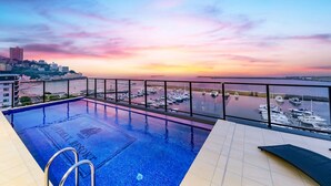 A rooftop infinity pool with a view of the marina and city skyline at sunset. - LiVEMAX RESORT ATAMI SEA FRONT (Atami)