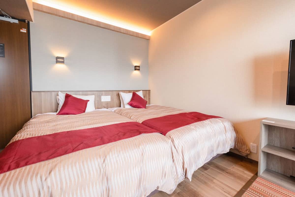 A double bed with red and beige bedding, a wooden headboard, and two wall-mounted lights.