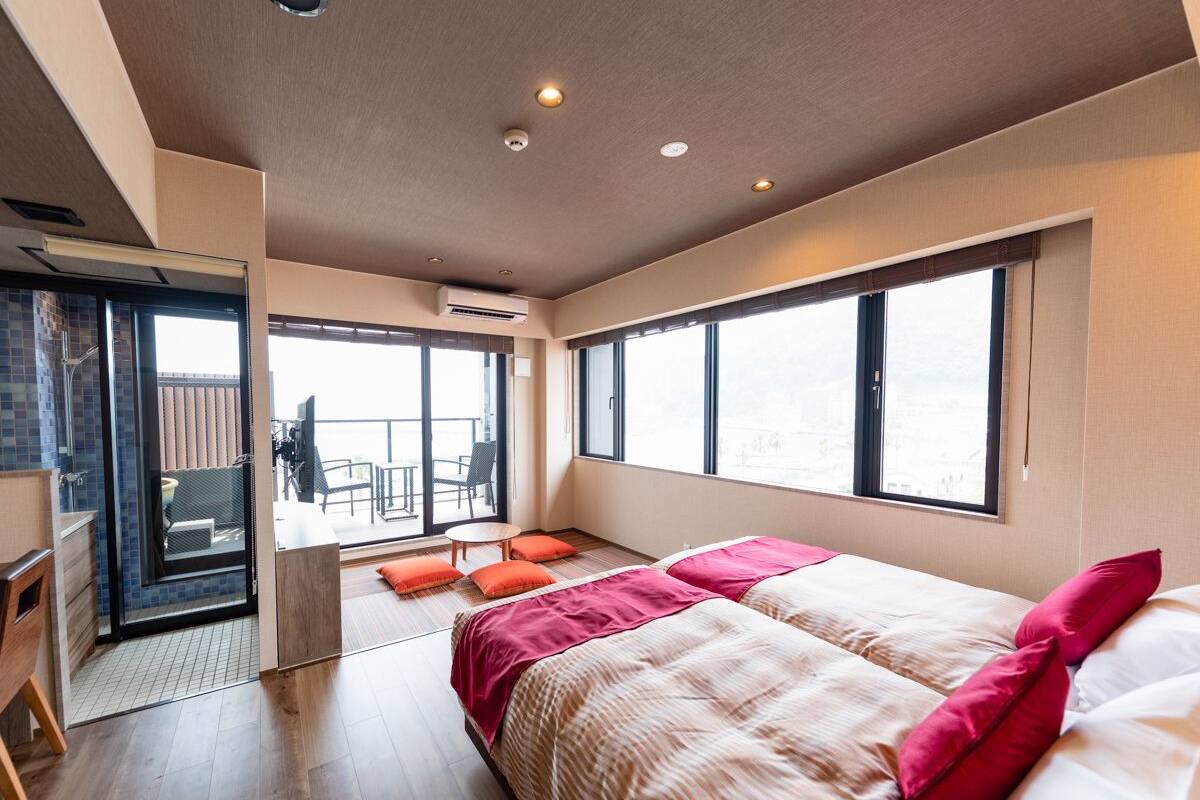 A modern hotel room with a large bed, a balcony with a view, and a sliding door to a balcony area.