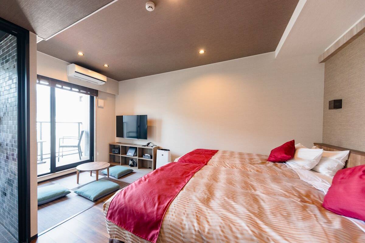 A modern hotel room with a large bed, a TV, a desk, and a balcony.