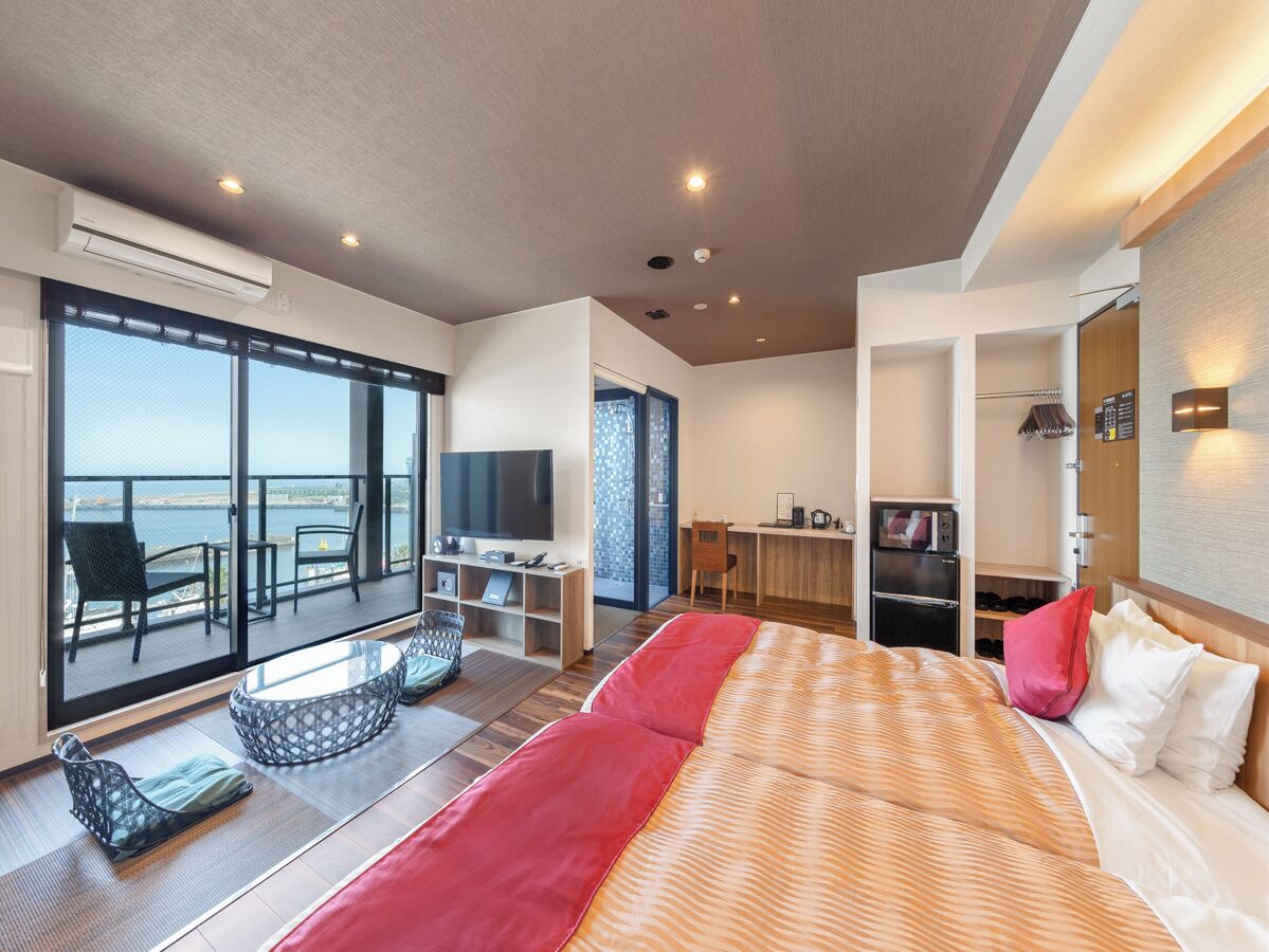 Et moderne hotelværelse med en stor seng, et fjernsyn, et skrivebord og en balkon med havudsigt.