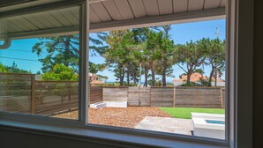 A view through a window of a backyard with a wooden fence, a lawn, and a patio area. - Pebble Beach Retreat • Ocean Views • Infrared Sauna • Short Walk to Beach (Del Monte Forest)