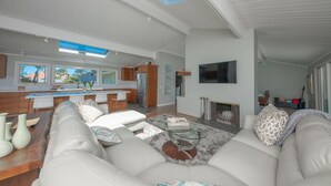 A modern living room with a sofa, coffee table, and a fireplace. There is a kitchen area with a dining table and chairs. - Pebble Beach Retreat • Ocean Views • Infrared Sauna • Short Walk to Beach (Del Monte Forest)