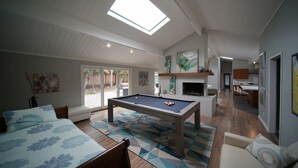 A spacious living room with a pool table, a sofa, and a dining area with a kitchen in the background. - Pebble Beach Retreat • Ocean Views • Infrared Sauna • Short Walk to Beach (Del Monte Forest)
