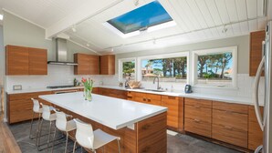 A modern kitchen with a central island, wooden cabinets, and a skylight. - Pebble Beach Retreat • Ocean Views • Infrared Sauna • Short Walk to Beach (Del Monte Forest)