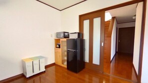 A small, clean room with a wooden floor, a black refrigerator, a microwave, and a small cabinet. - Wakayama House No.7 (Wakayama)