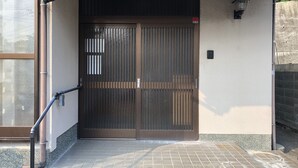 A gated entrance with a metal gate, a tiled step leading up to the gate, and a wall-mounted light fixture to the right. - Wakayama House No.10 (Wakayama)