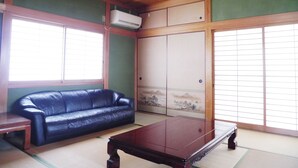 A traditional Japanese room with tatami flooring, a black leather sofa, a wooden coffee table, and sliding shoji doors. - Wakayama House No.10 (Wakayama)