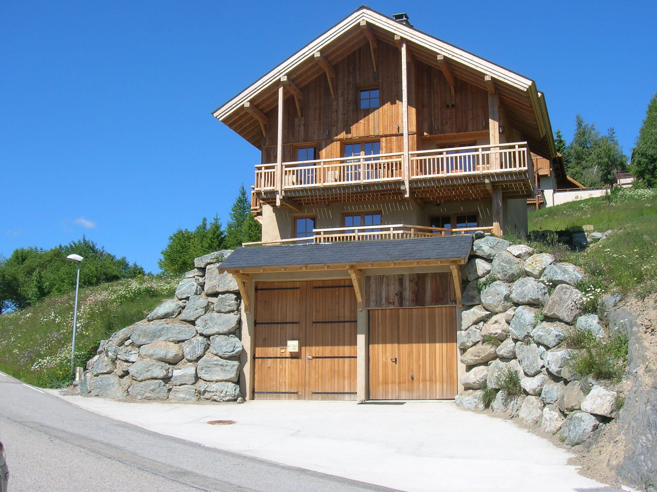 A two-story wooden cabin with a balcony, stone walls, and a garage.