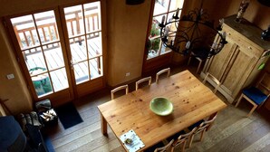 Uma mesa de jantar de madeira com cadeiras, uma janela grande e um candelabro.