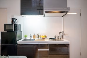 A compact kitchen with a microwave, refrigerator, sink, and a small countertop with various kitchen items. - Grandouce Daikokucho (Osaka)