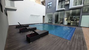 A modern outdoor swimming pool area with wooden decking and lounge chairs.