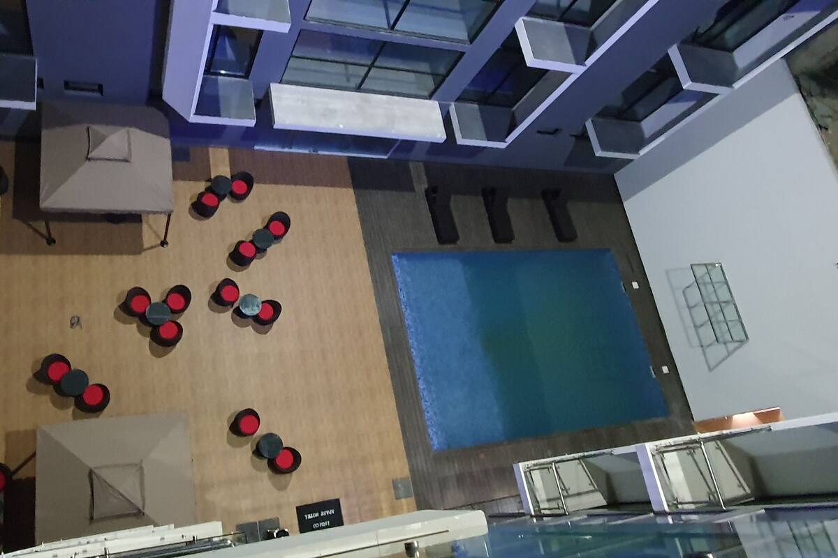 A room with a wooden floor, several tables with chairs, a pool, and a glass railing.