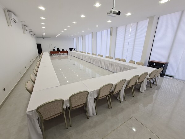 A conference room with a long table, chairs, a projector, and large windows. - Indico Executivo Hotel (Nacala)