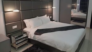 A modern bedroom with a large bed, a nightstand, a mirror, and a built-in wardrobe.