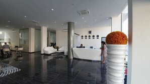 A modern hotel lobby with a reception desk, seating area, and a large decorative vase.