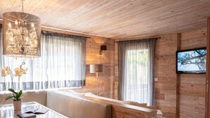 Una sala de estar moderna con techo de madera, una mesa de comedor con superficie de vidrio y un banco, un sofá y un televisor fijado a la pared.