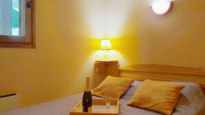 Een bed met houten hoofdbord, twee kussens, een nachtkastje met lamp en een dienblad met fles en glazen.