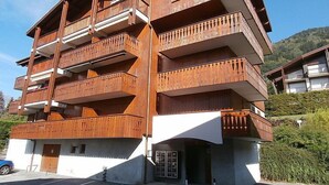 Een meerhoog gebouw met balkons, een parkeerplaats en een bergachtige achtergrond.