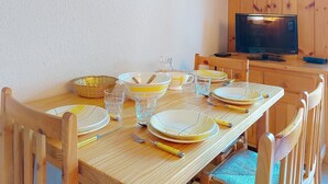 Een houten eettafel gedekt met borden, glazen en bestek, met een televisie en houten lambrisering op de achtergrond.