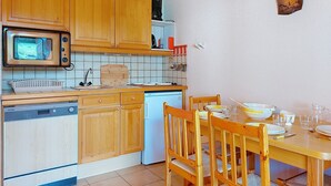 Een keuken met houten kastjes, een magnetron, een vaatwasser en een eettafel gedekt met borden en glazen.