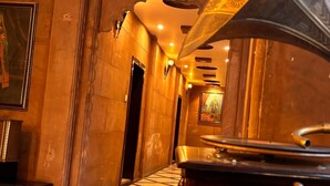 Un piano de cola en el vestíbulo de un hotel, con suelo de mármol, una escalera y un cuadro en la pared.