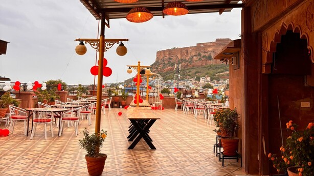 Una terraza exterior con lámparas de mimbre, sillas blancas y plantas en macetas.