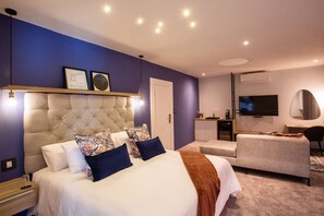 A modern bedroom with a large bed, bedside tables, a desk, a chair, a TV, and a mirror.