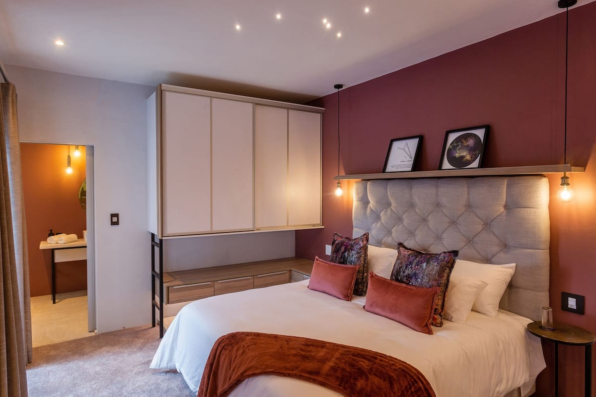 A bedroom with a large bed, a wardrobe, a bedside table, and a mirror.