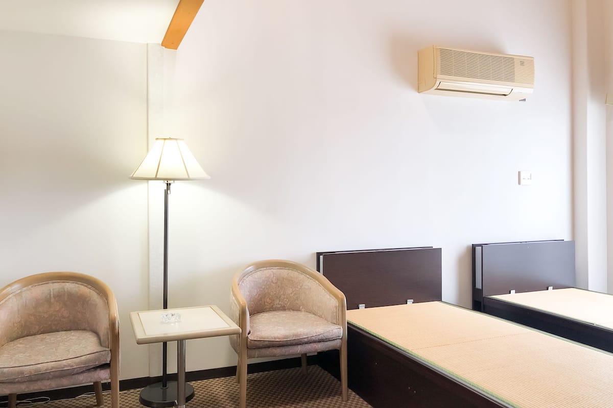 Hotellihuoneessa on kaksi tuolia, pieni pöytä, sänky ja seinälle asennettu ilmastointilaite.