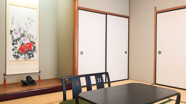 Een traditionele Japanse kamer met tatami vloerbedekking, een lage tafel en een schilderij van bloemen en vogels.