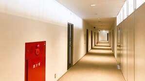 Hotelhal met een brandmelder aan de linkerkant, deuren aan beide zijden en een vloerbedekking.
