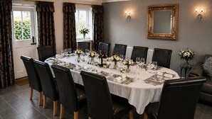 Une salle à manger avec une longue table dressée pour un repas, des chaises noires, un miroir et un vase rempli de fleurs.