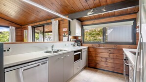 A modern kitchen with wooden ceiling, built-in appliances, and large windows. - Sensational Sun Trap on Estuary Frontage - Pauanui (Pauanui)