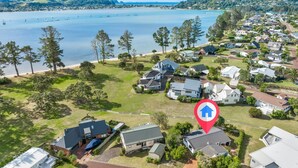 An aerial view of a coastal residential area with houses, a clear view of the sea, and a prominent red location marker. - Sensational Sun Trap on Estuary Frontage - Pauanui (Pauanui)