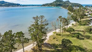 A coastal landscape with a beach, clear blue water, and a hill with houses. - Sensational Sun Trap on Estuary Frontage - Pauanui (Pauanui)