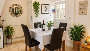 A dining area with a table set for four, chairs, a potted plant, a framed artwork, and a mirror on the wall. - Juliet Cottage (Stratford-upon-Avon)