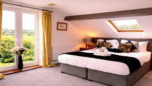 A bedroom with a large bed, a skylight, a view of greenery, a bedside table with a lamp, and a radiator. - Juliet Cottage (Stratford-upon-Avon)