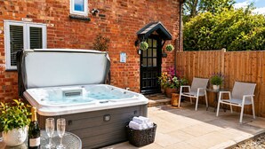 A hot tub in a backyard with a brick house, outdoor seating, and potted plants. - Juliet Cottage (Stratford-upon-Avon)