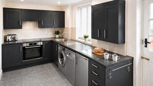 Una cocina moderna con armarios negros, horno empotrado, lavadora y una encimera con un tostador, un pan y dos tazas.